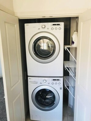 A laundry room with two stacked LG washing machines and a shelf with a bottle. - Modern Apt #402 - a Block from St Pat's Hospital (Missoula)