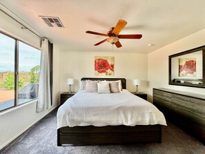 A hotel room with a bed, two bedside tables, a ceiling fan, a large window, and artwork on the walls. - Dove Mountain #12361 (Marana)
