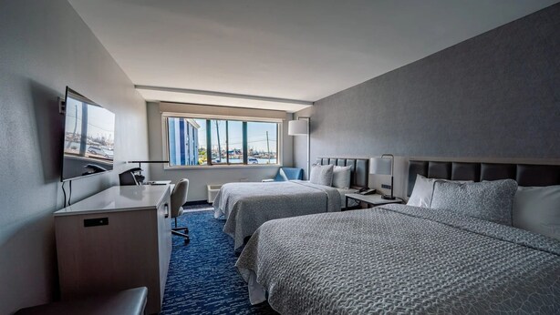 Habitación de hotel con dos camas, un escritorio, una silla, un televisor y una ventana con vistas a la ciudad.