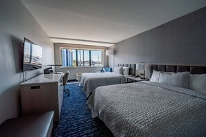 Une chambre d’hôtel avec deux lits, un bureau, une chaise, une télévision et une fenêtre donnant sur la ville.