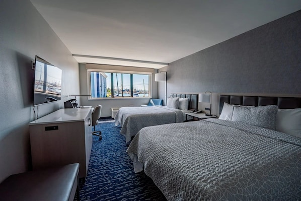 Une chambre d’hôtel avec deux lits, un bureau, une chaise, une télévision et une fenêtre donnant sur la ville.