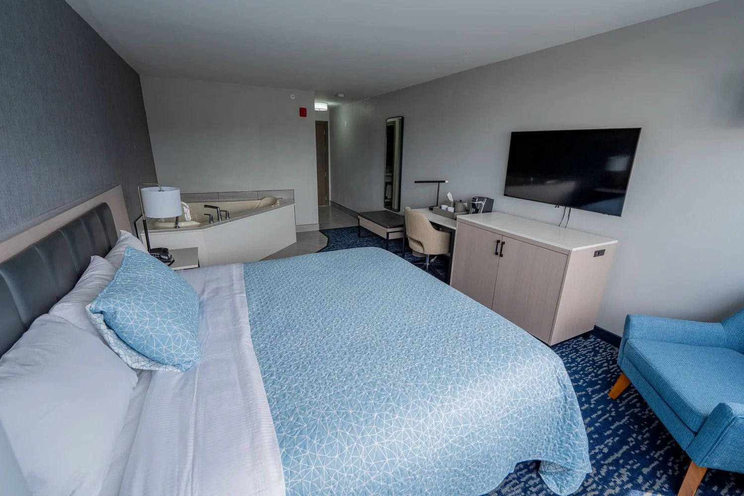 Quarto de hotel com cama, escrivaninha, cadeira, televisão e banheiro.