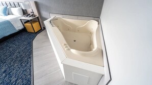 A modern bathroom with a freestanding bathtub, a bedside table with a lamp, and a bed with a blue patterned bedspread. - Harbor View - King Bed With Jacuzzi (Fiarhaven)