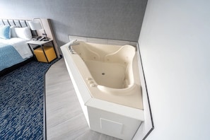 Un baño moderno con una bañera independiente, una mesita de noche con lámpara y una cama con colcha estampada azul.