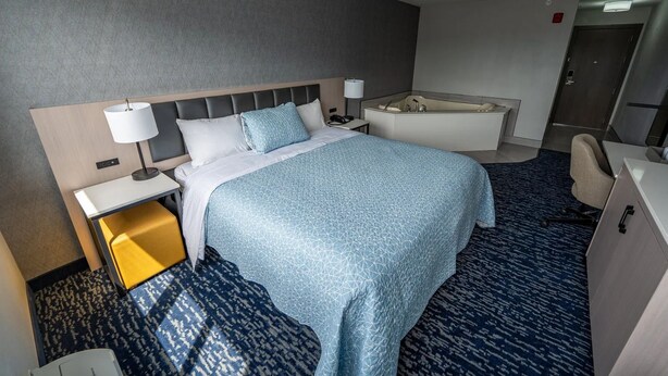 A hotel room with a bed, bedside table, lamp, and a bathroom with a bathtub. - Harbor View - King Bed With Jacuzzi (Fiarhaven)