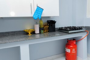Uma bancada de cozinha com fogão a gás, um extintor de incêndio vermelho, uma tigela dourada, um rolo de papel toalha, uma garrafa de óleo e um porta-utensílios preto.