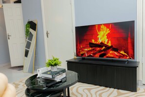 A living room with a flat-screen TV, a fireplace, a potted plant, and a book on a glass coffee table. - Modern living with a cozy design, a place where you can relax and feel like home (Dar es Salaam)