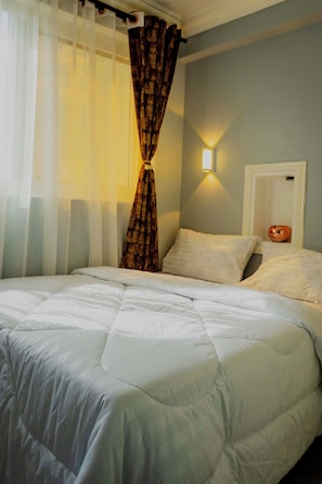 A bed with a white duvet, a wall-mounted light, and a curtain. - Modern living with a cozy design, a place where you can relax and feel like home (Dar es Salaam)