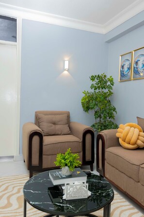 A living room with a beige armchair, a round coffee table with a plant, and a wall-mounted light fixture. - Modern living with a cozy design, a place where you can relax and feel like home (Dar es Salaam)