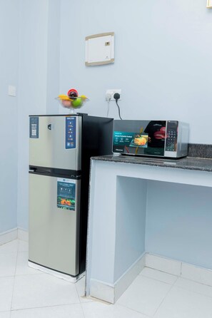 A compact kitchenette with a stainless steel refrigerator, a microwave, and a bowl of fruit on the counter. - Modern living with a cozy design, a place where you can relax and feel like home (Dar es Salaam)