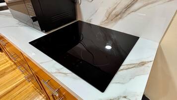 A kitchen with a black induction cooktop on a white marble countertop, wooden cabinets below, and a marble backsplash.