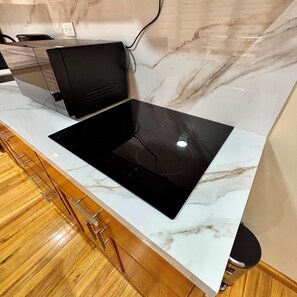 A kitchen with a black induction cooktop on a white marble countertop, wooden cabinets below, and a marble backsplash. - Hotel Boutique Celines (Cuenca)