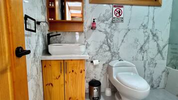 A bathroom with a marble wall, a wooden cabinet, a sink, a toilet, and a window with a view of greenery.