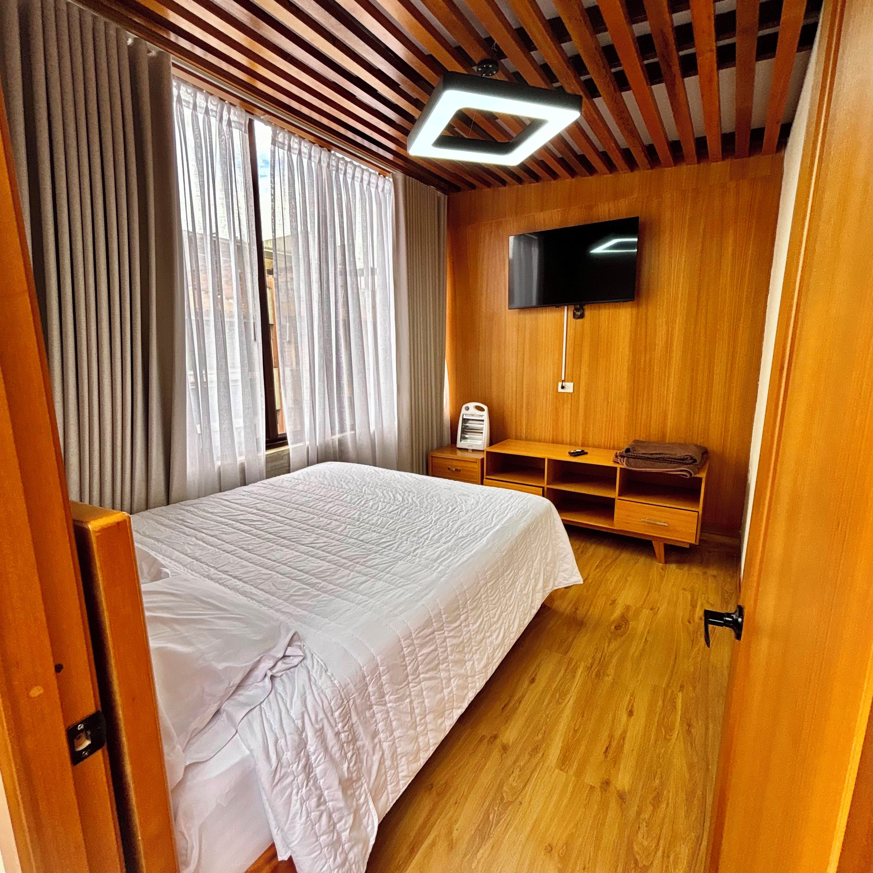 Une chambre à coucher avec un lit, un téléviseur fixé au mur et un plancher en bois.