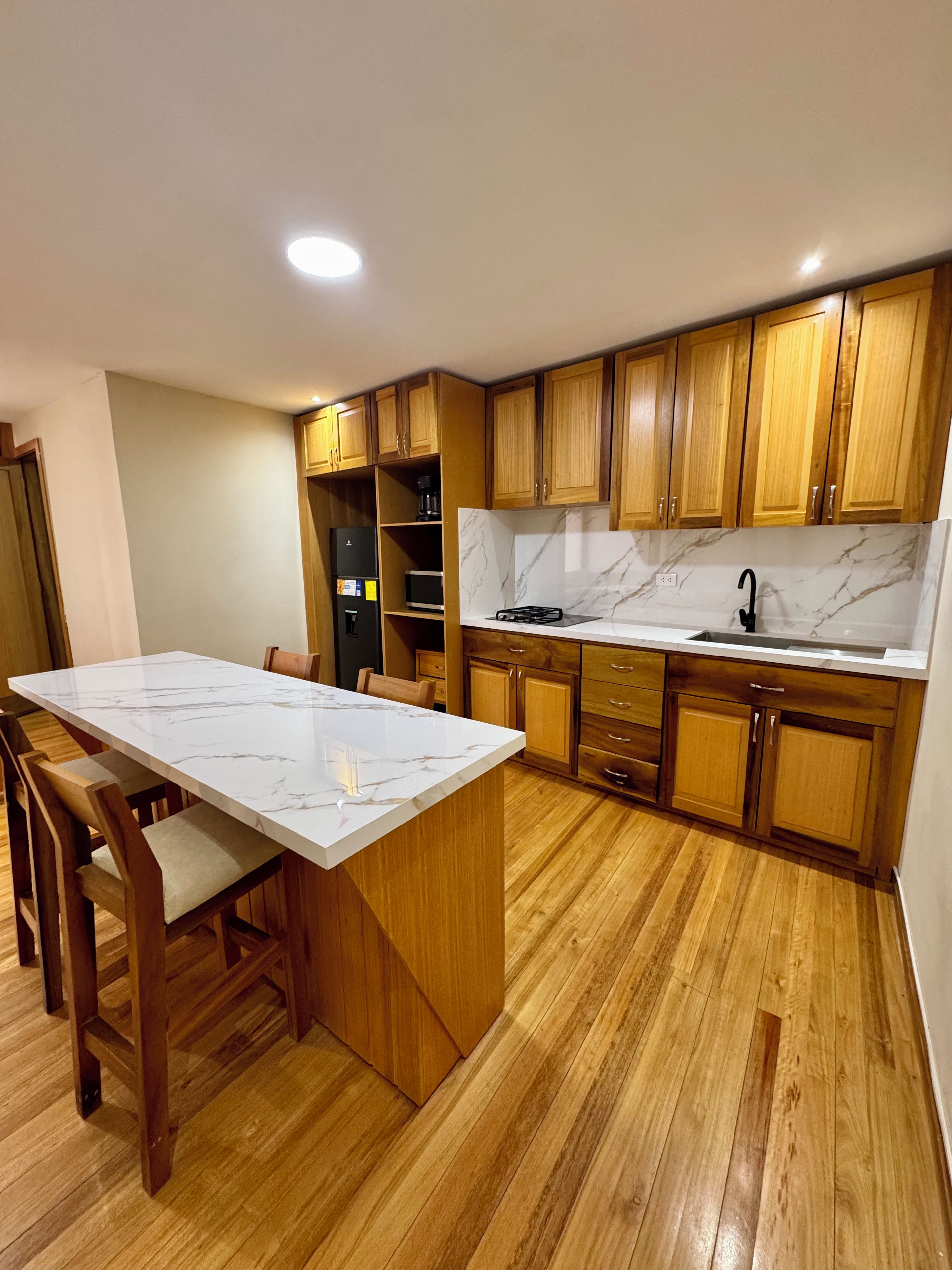 Una cocina con armarios de madera, encimera de mármol y una isla central con sillas.