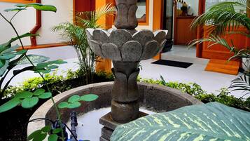 Une fontaine en pierre à plusieurs niveaux, entourée de plantes en pot, se trouve dans un hall d’entrée avec un comptoir de réception et une enseigne indiquant « CELINES ».
