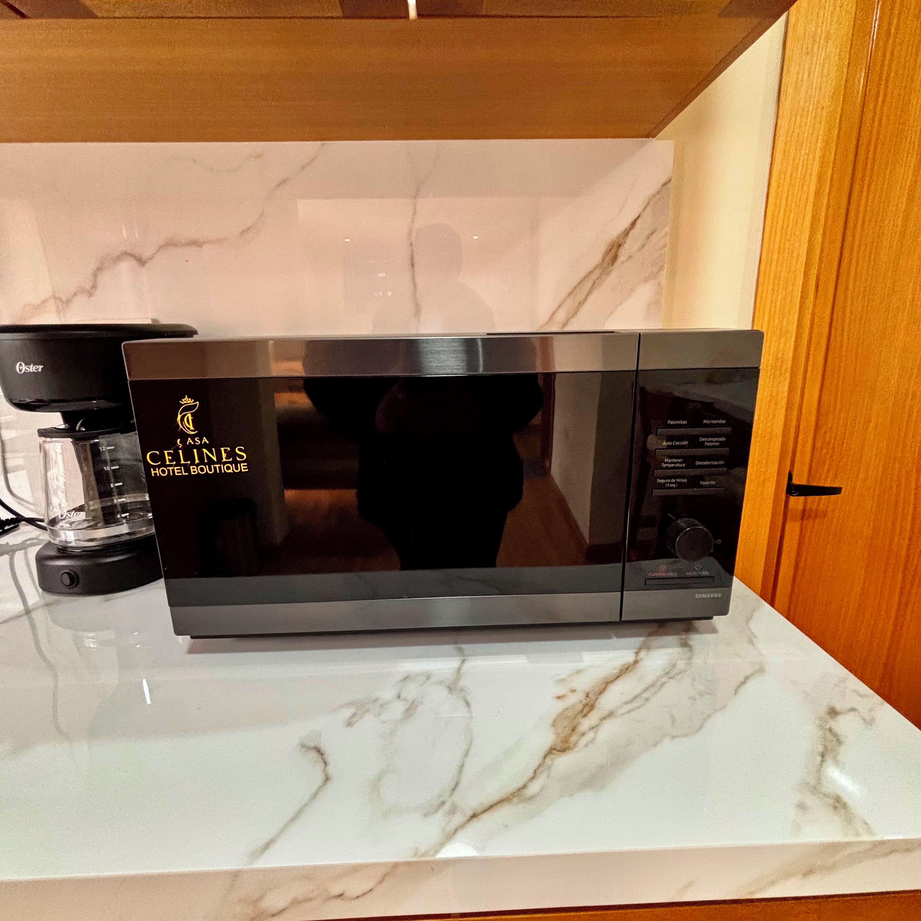 Une cuisine moderne équipée d’un four à micro-ondes en acier inoxydable, d’une machine à café et d’un plan de travail en marbre.