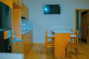 A compact kitchen with wooden cabinets, a white countertop, and a small dining table with two chairs. - Hotel Boutique Celines (Cuenca)