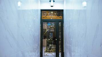 Entrada de hotel con pared de mármol, una puerta metálica y un candelabro colgante.