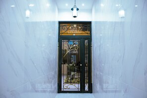 Entrada de hotel con pared de mármol, una puerta metálica y un candelabro colgante.