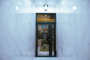 Entrada de hotel con pared de mármol, una puerta metálica y un candelabro colgante.