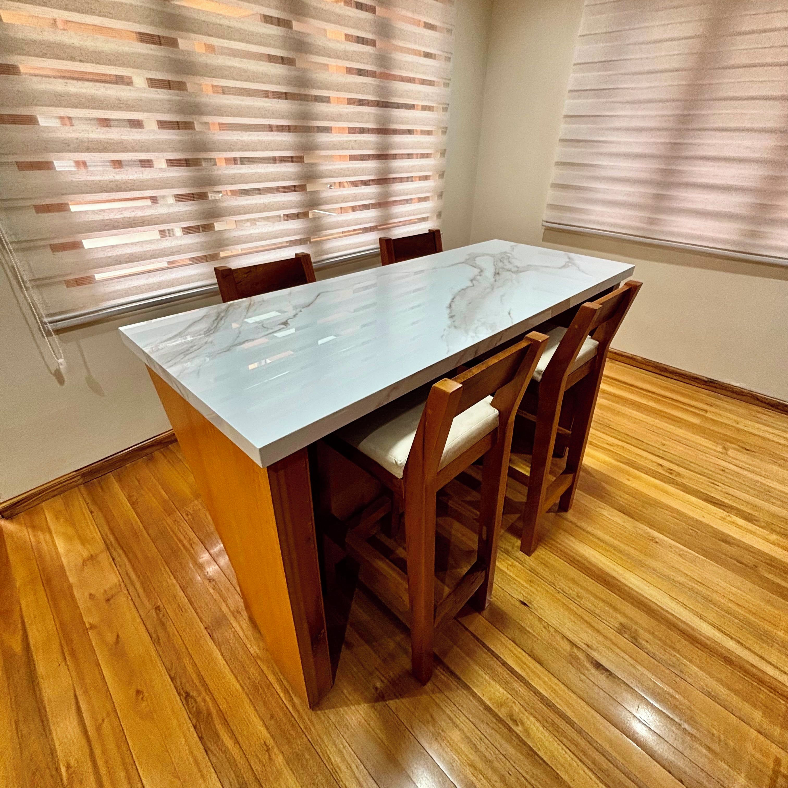 Une table à manger avec un plateau en marbre, entourée de chaises en bois dotées d’assises rembourrées, le tout posé sur un plancher en bois.