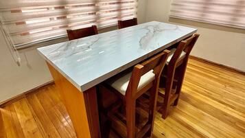 Une table à manger avec un plateau en marbre, entourée de chaises en bois dotées d’assises rembourrées, le tout posé sur un plancher en bois.