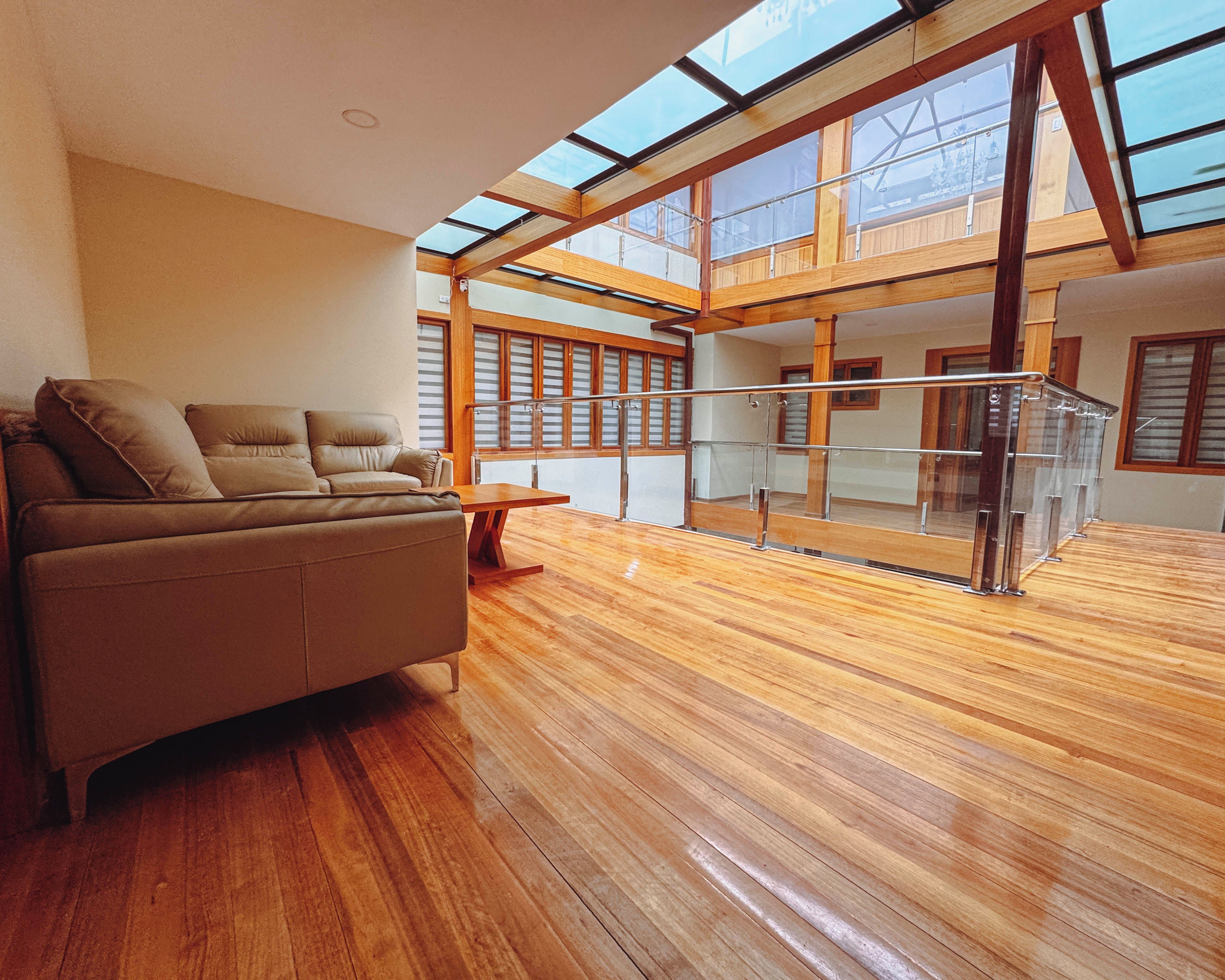 Una habitación amplia con suelo de madera, un sofá y una barandilla de cristal con vistas a un balcón.