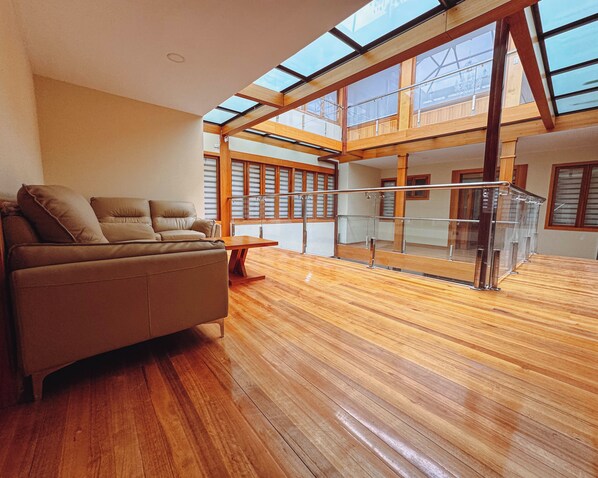 Una habitación amplia con suelo de madera, un sofá y una barandilla de cristal con vistas a un balcón.