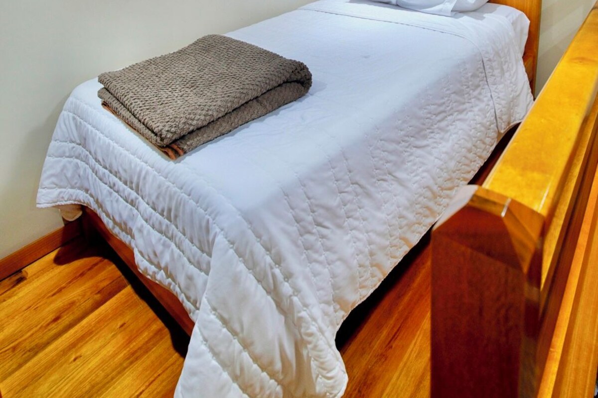 A single bed with a wooden headboard, a white mattress, and a brown blanket.
