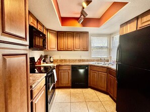 A kitchen with wooden cabinets, a black refrigerator, a dishwasher, and a microwave. - Greens at Ventana Canyon #13104 (Catalina Foothills)
