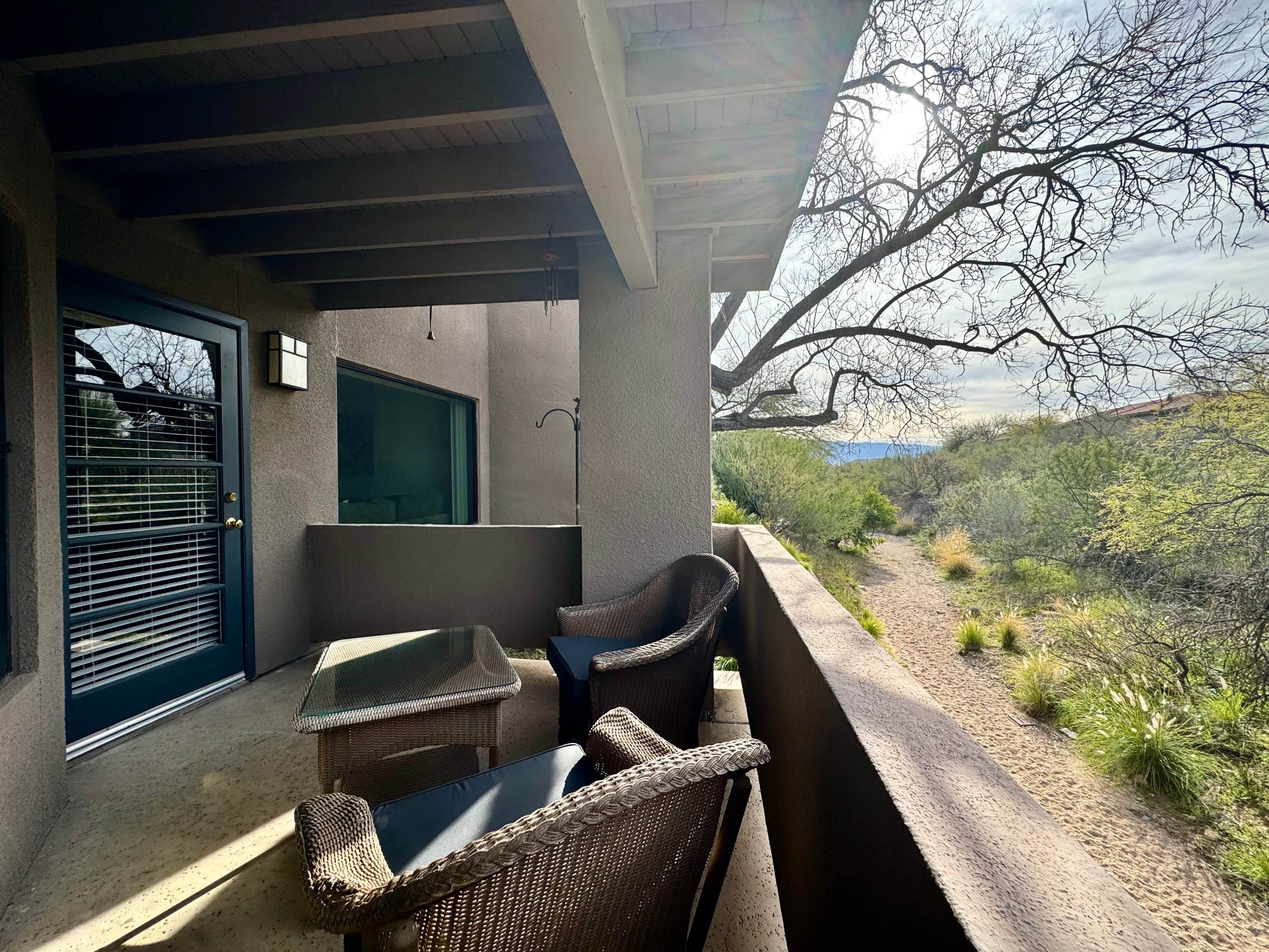 A covered outdoor seating area with wicker furniture and a view of a natural landscape.