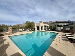 A swimming pool with a clear blue water, surrounded by lounge chairs and a barbecue area, with mountains in the background. - Greens at Ventana Canyon #13104 (Catalina Foothills)