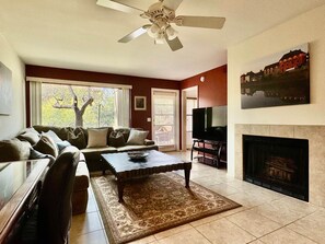 A living room with a sofa, coffee table, fireplace, television, and a ceiling fan. - Greens at Ventana Canyon #13104 (Catalina Foothills)