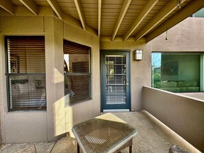 A covered outdoor area with a wicker table, a door, and windows with blinds. - Greens at Ventana Canyon #13104 (Catalina Foothills)