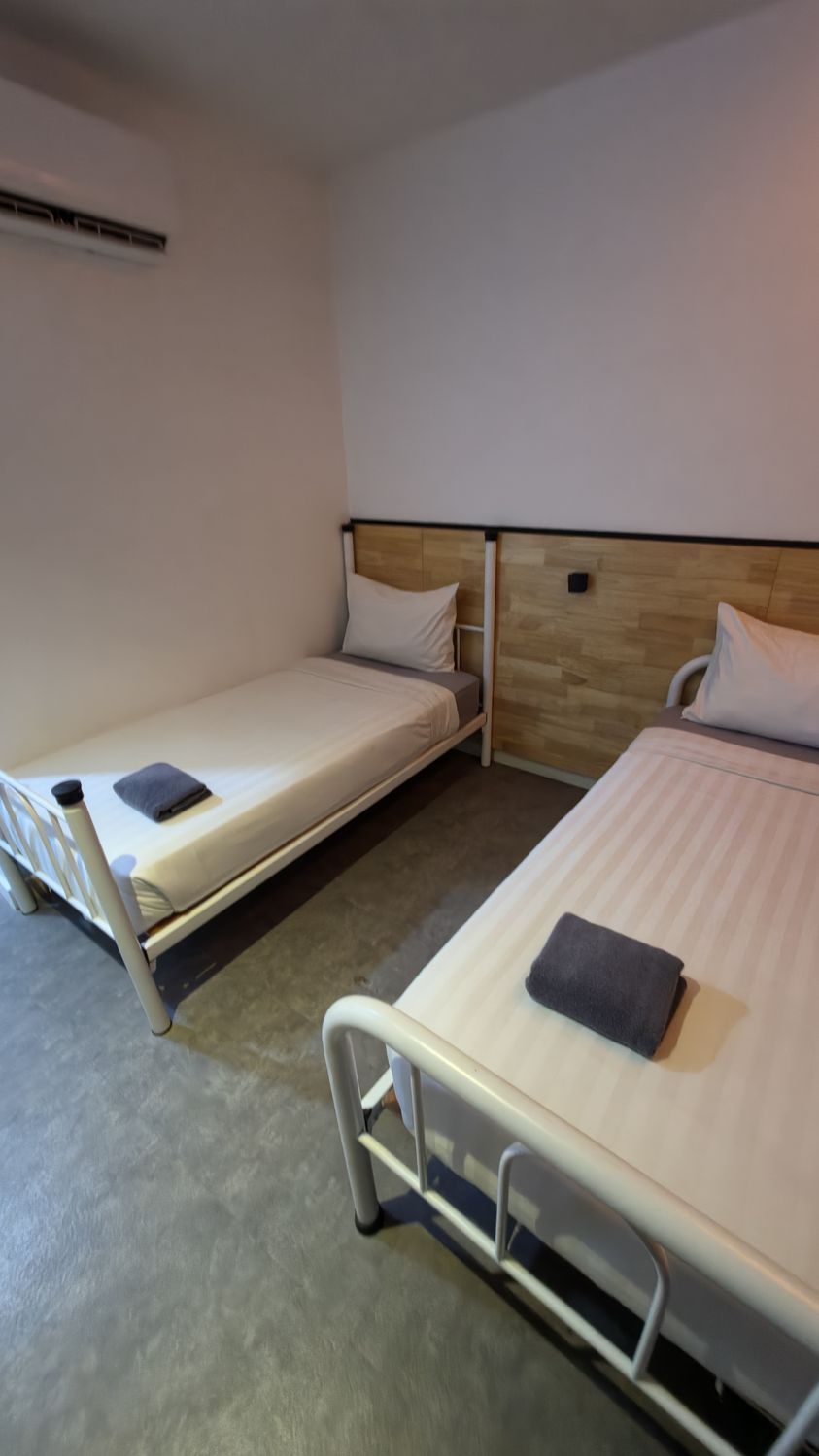 Habitación de hotel con dos camas individuales, cabecera de madera, mesita de noche pequeña y aire acondicionado instalado en la pared.