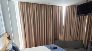 A hotel room with a bed, a sofa, a television, and curtains.