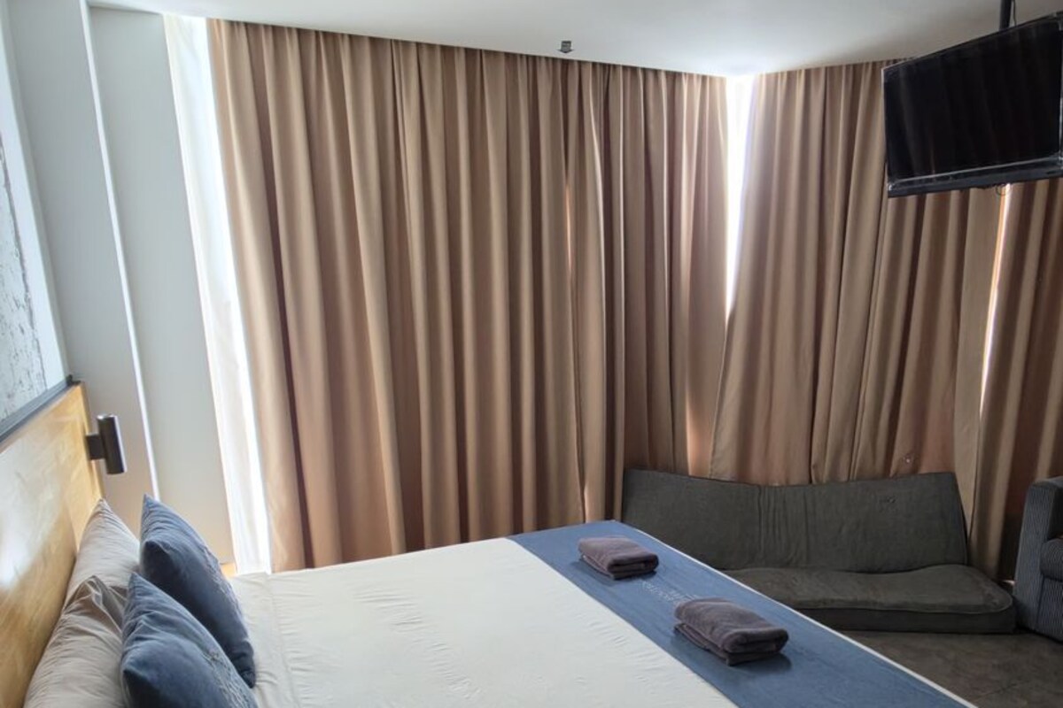 Ett hotellrum med en säng, en soffa, en tv och gardiner.