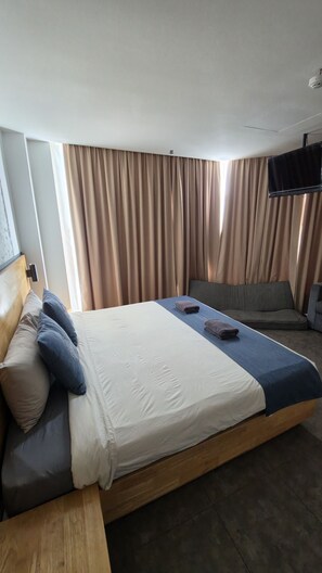 Habitació d'hotel amb un llit, un sofà, televisió de pantalla plana i cortines.