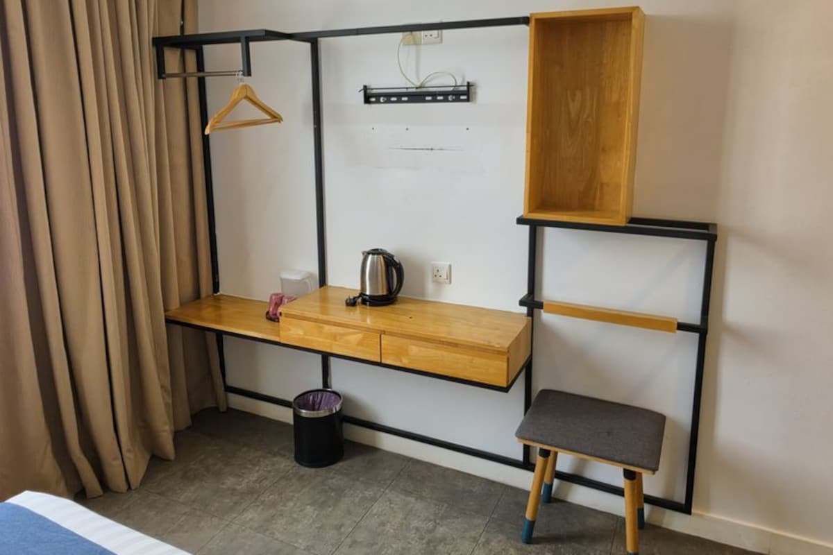 Habitació d'hotel amb llit, escriptori, llum penjant i un petit cub de basures.