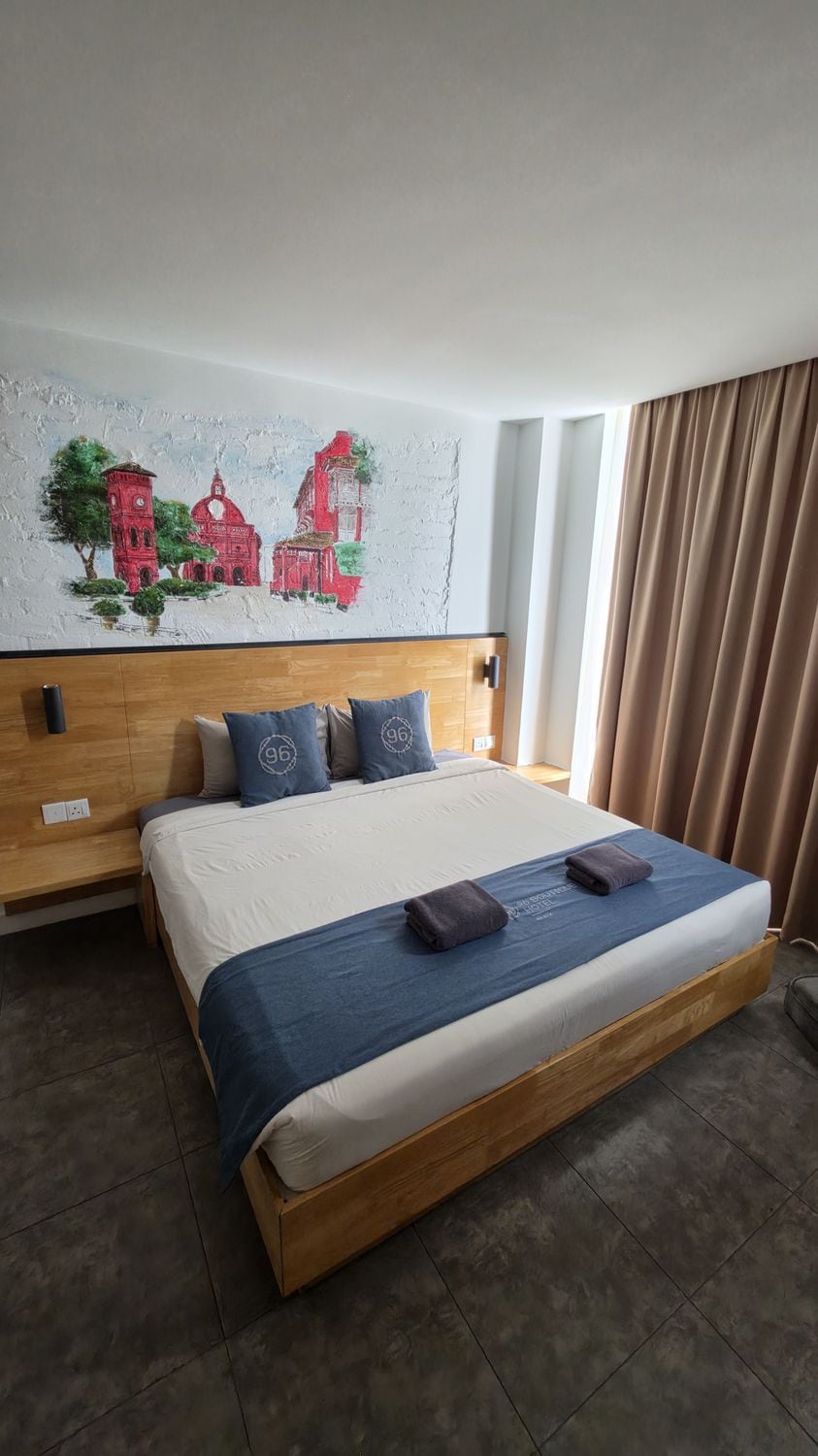 Una habitación de hotel con una cama grande, un cabecero de madera, un mural en la pared y una ventana con cortinas.