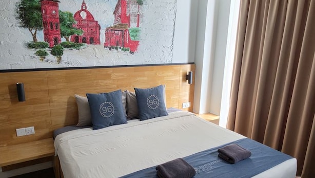 A hotel room with a large bed, a headboard with a wooden finish, a wall mural, and a window with curtains.