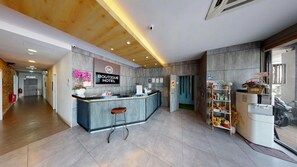 Zona d'entrada d'un hotel amb un disseny modern, incloent un taulell de recepció, una zona de bar i un bar de tapes.