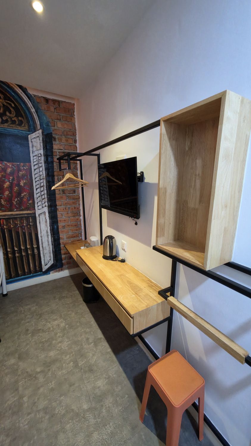 A compact room with a wooden desk, a black TV mounted on the wall, and a small orange stool.