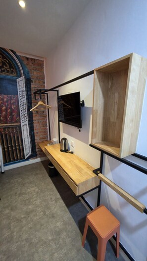 Una habitación compacta con un escritorio de madera, un televisor negro montado en la pared y un taburete naranja pequeño.