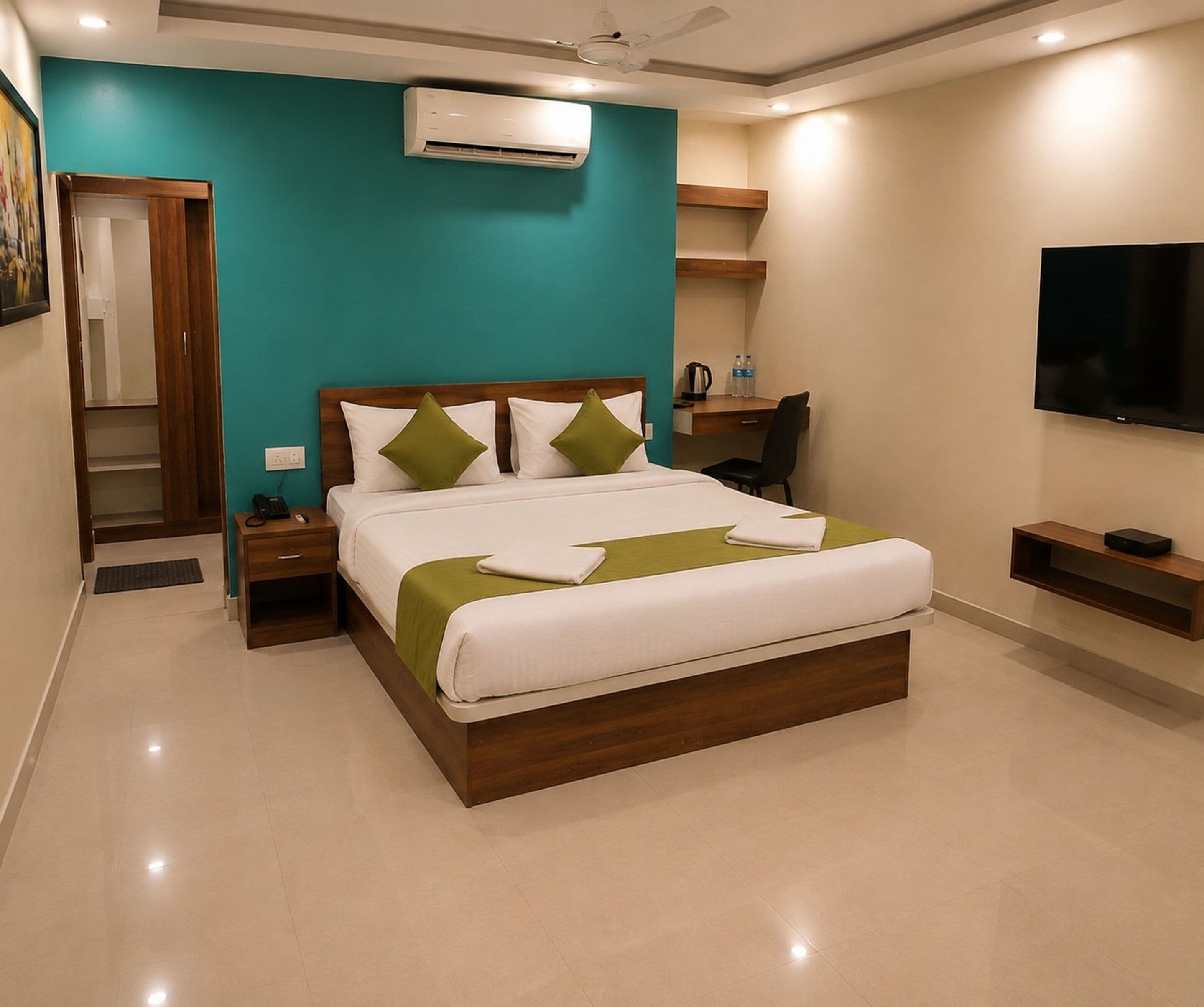 A hotel room with a bed, bedside tables, a desk, a chair, an air conditioning unit, a television, and a wardrobe.