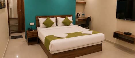 A hotel room with a bed, bedside tables, a desk, a chair, an air conditioning unit, a television, and a wardrobe.
