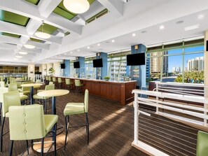 En modern hotellobby med en bardel, sittgrupper och stora fönster med utsikt över staden.