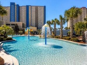 Ein Swimmingpool mit einer Wassersäule, umgeben von Palmen und Hotels im Hintergrund.