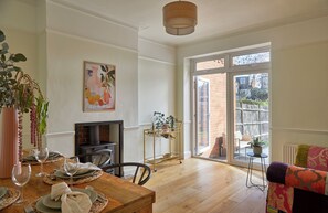 Un comedor con mesa de madera dispuesta para dos personas, una chimenea y vistas al exterior a través de un gran ventanal corredero.